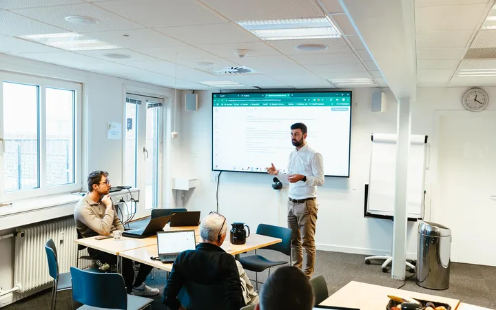 Jacob faciliterer en workshop om AI orchestratoren med kolleger og laptops i et lyst mødelokale